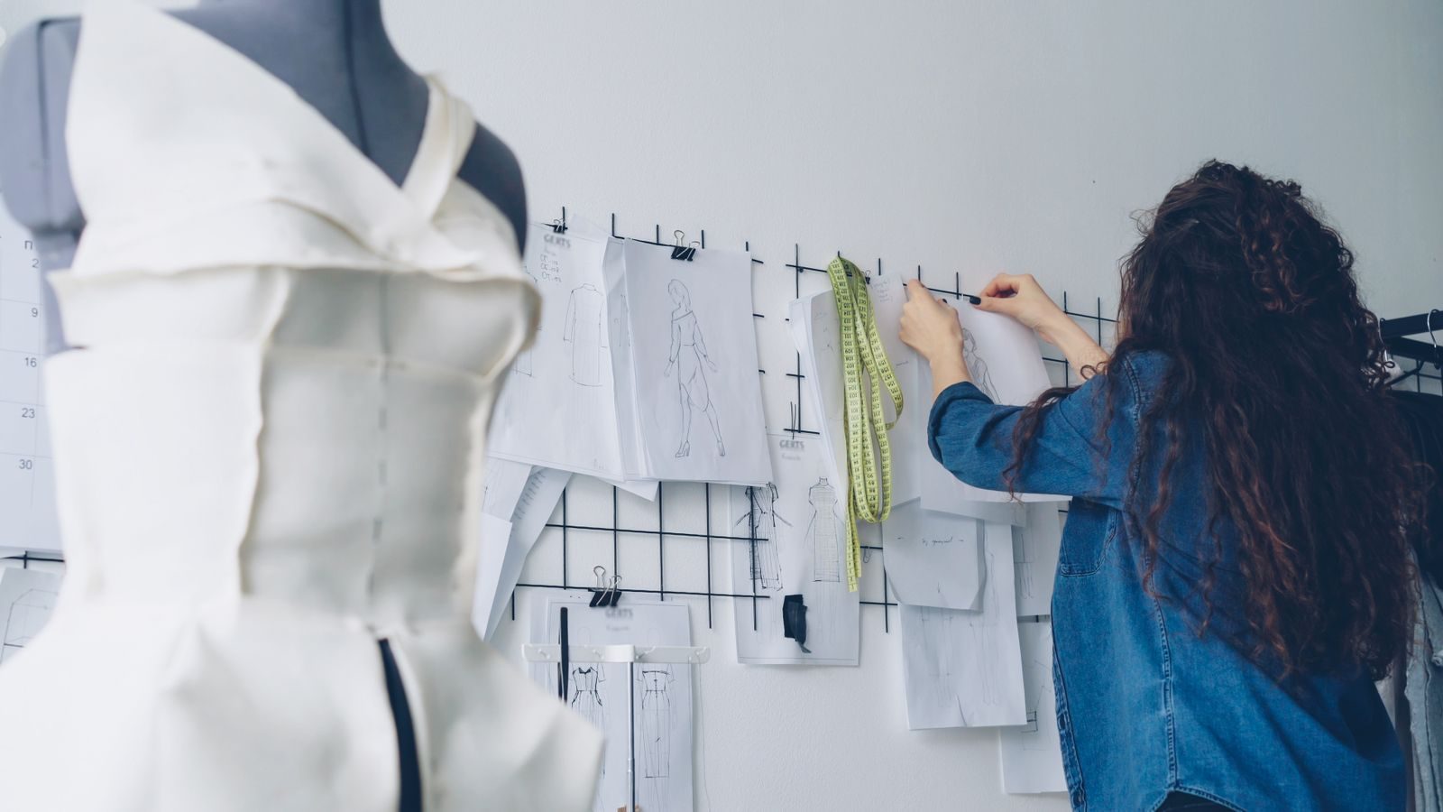 Estilista ajustando moldes em um painel de inspiração em um ateliê moderno