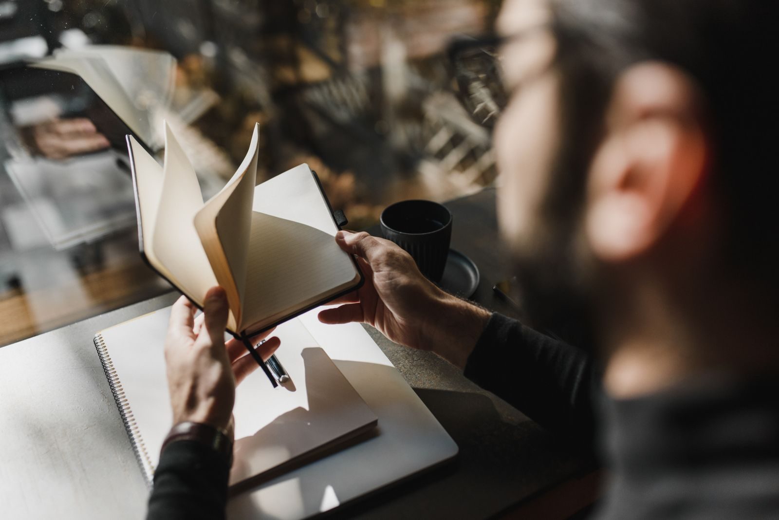 Pessoa folheando um caderno sentada perto de uma janela, em um ambiente aconchegante