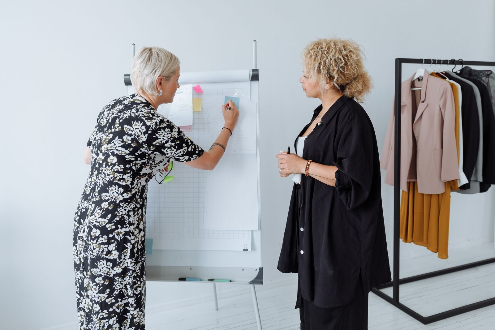 Duas mulheres trabalham juntas em conceitos de moda com um quadro e uma arara de roupas