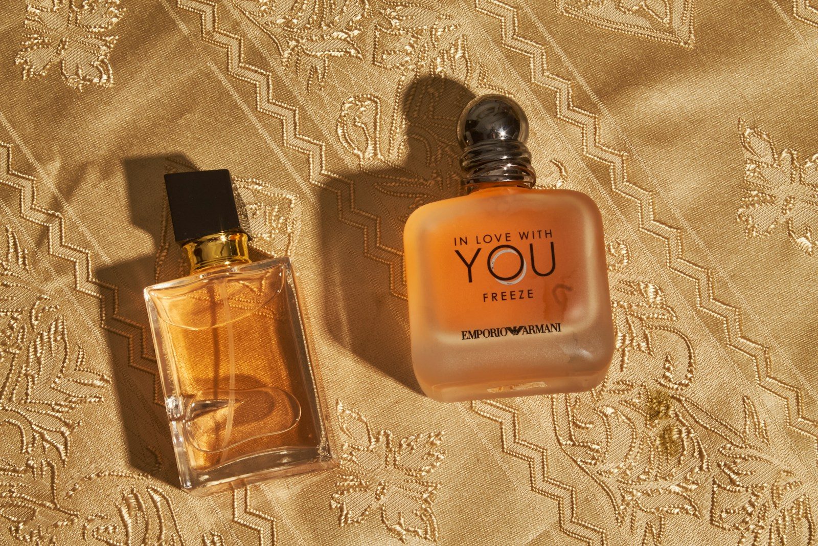 Dois frascos de perfume sobre tecido dourado estampado