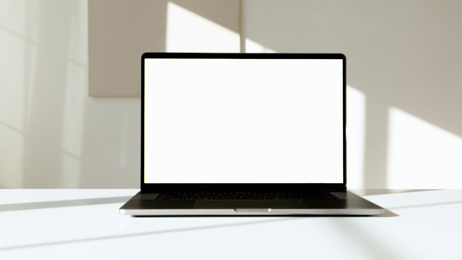 Notebook com tela branca em uma mesa, banhado por luz natural