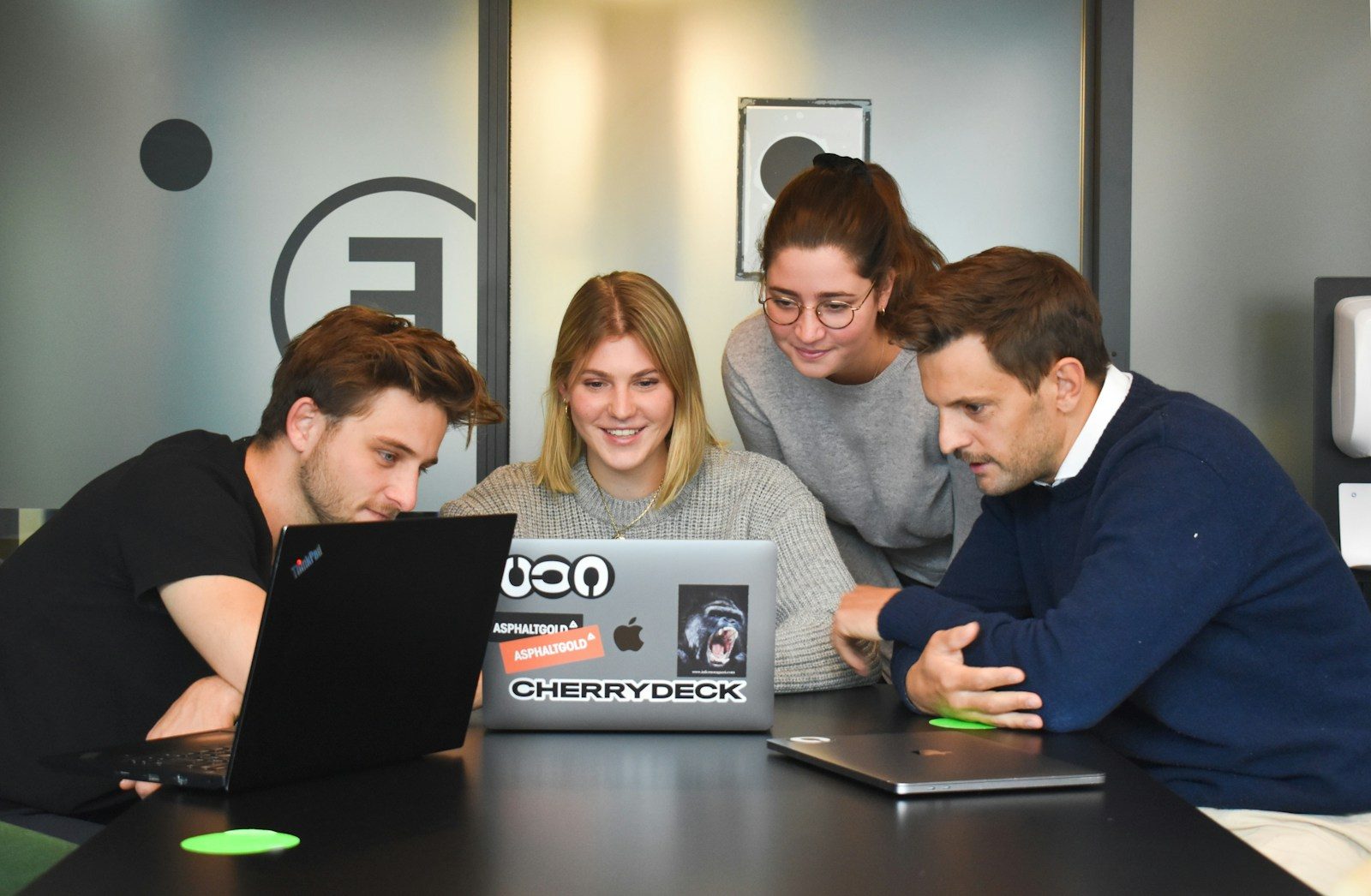 Quatro pessoas colaborando em torno de um laptop em um escritório moderno