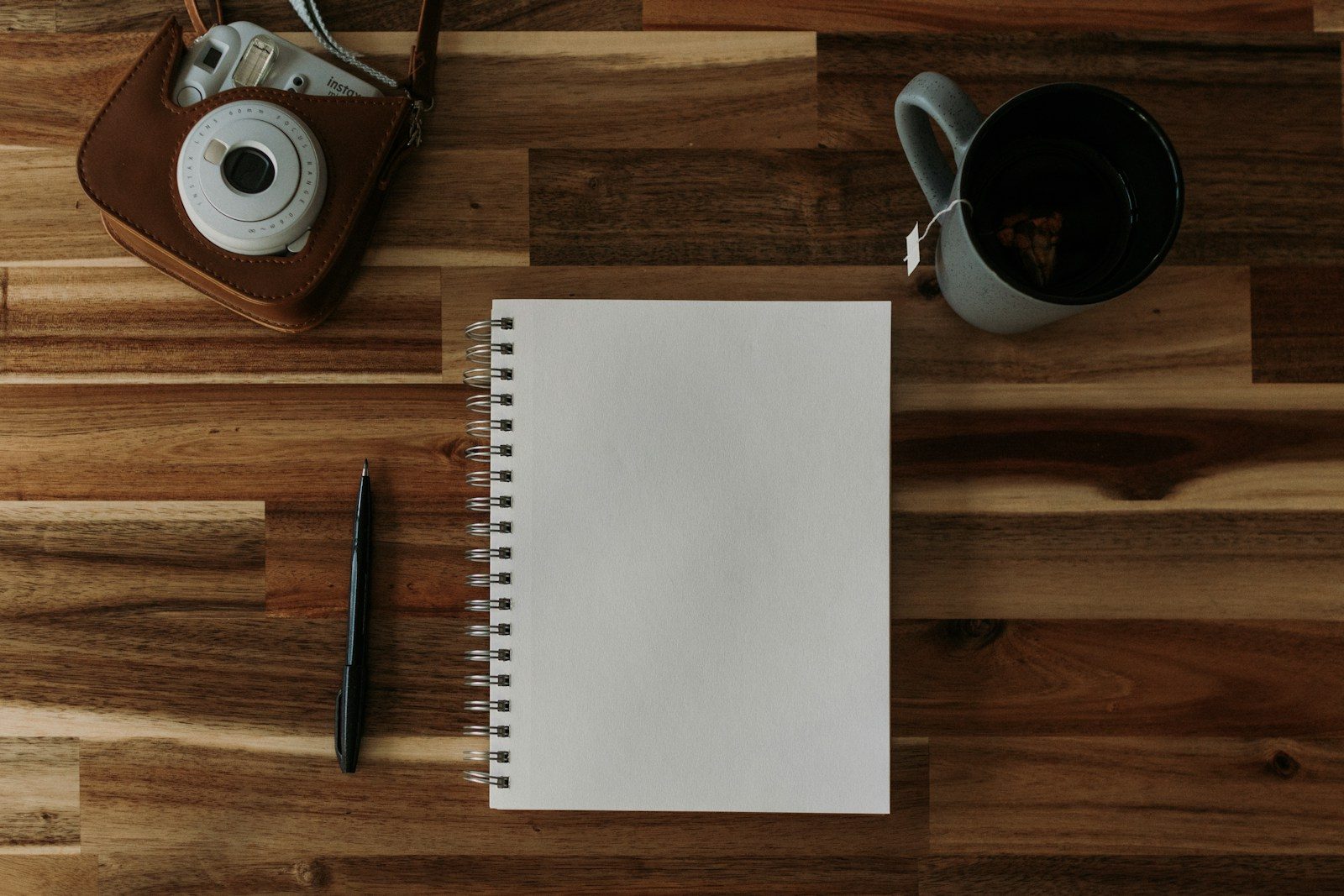 Bloco de notas, caneta, câmera e uma xícara de café em uma mesa de madeira