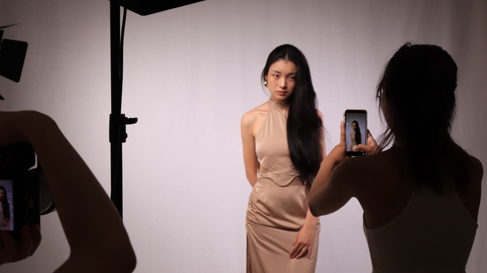 Ensaio profissional em estúdio de mulher de vestido bege, com câmeras digitais e smartphones