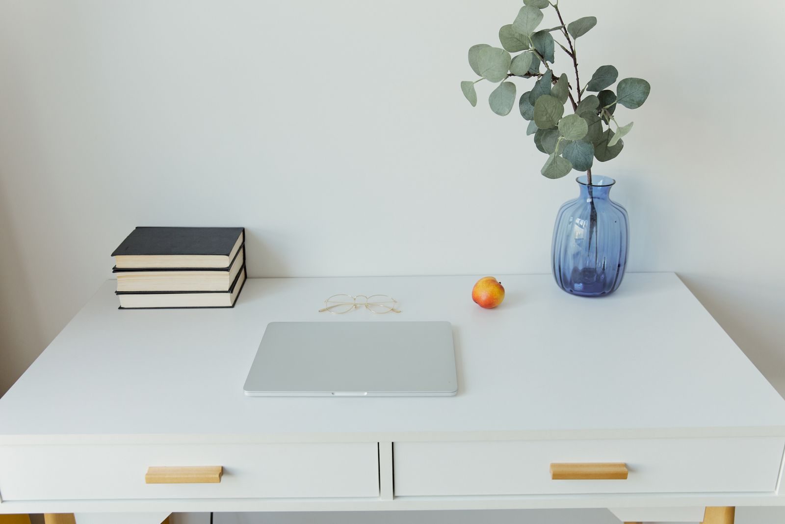 Mesa limpa e minimalista com notebook, livros e um vaso azul em um espaço de trabalho moderno