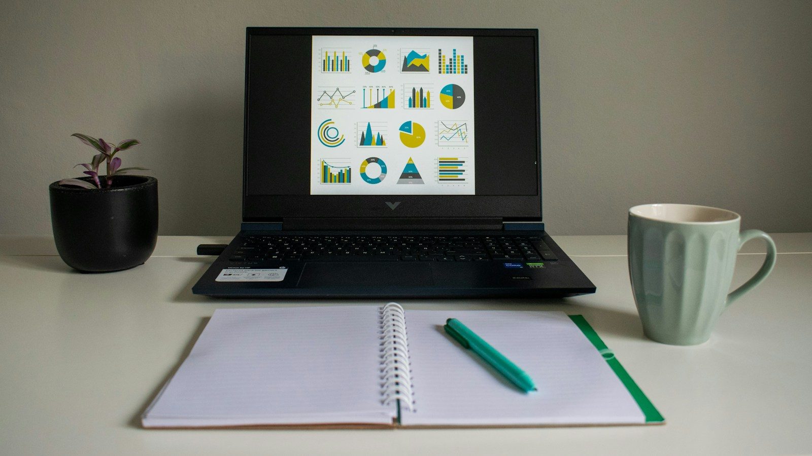 Notebook exibindo gráficos ao lado de caderno e caneca