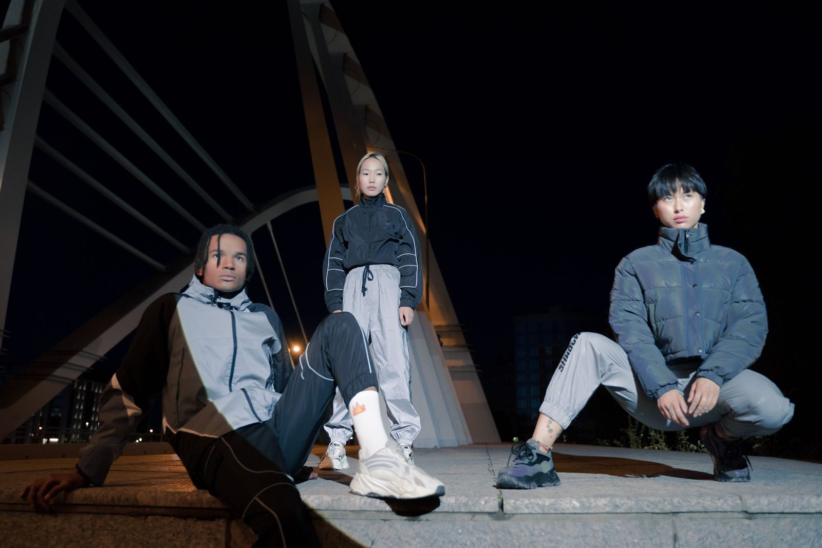 Grupo estiloso com roupas urbanas posa em uma ponte moderna à noite
