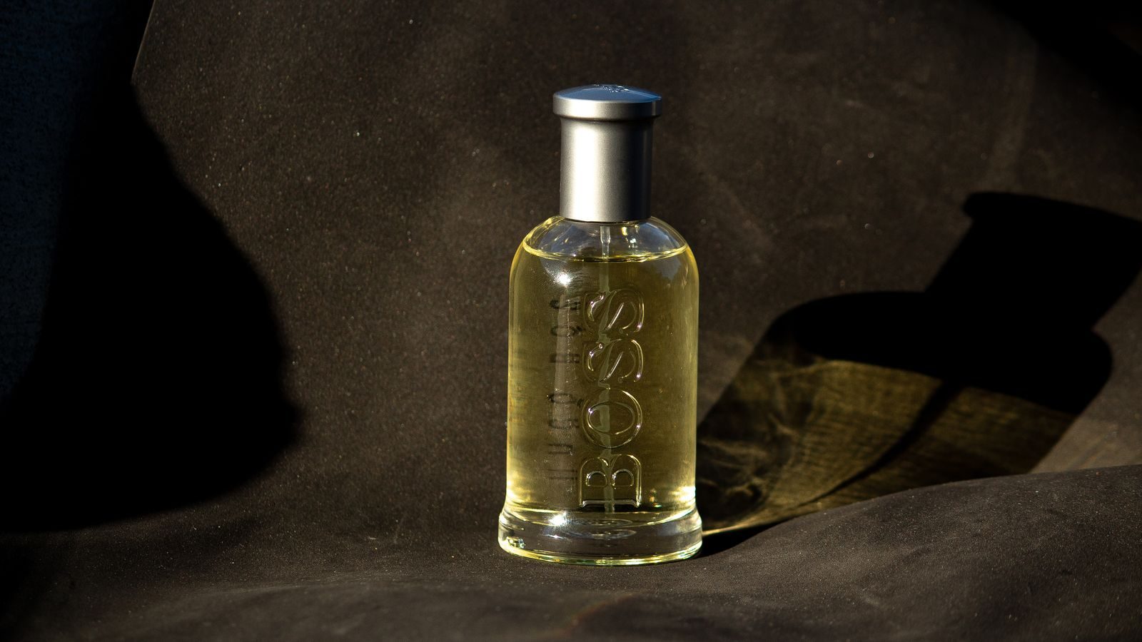Frasco de perfume sofisticado com texto em relevo sobre tecido escuro