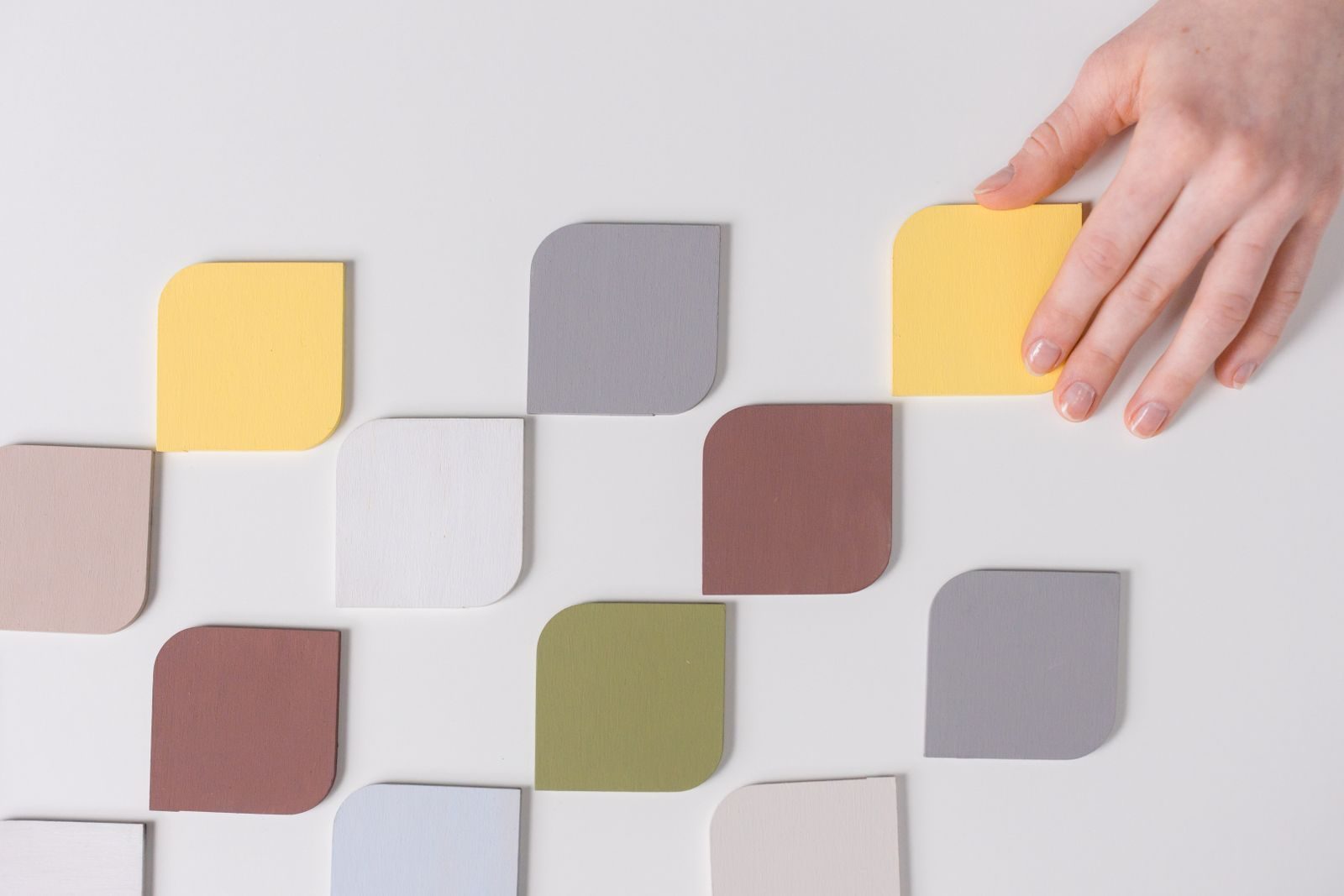 Mão organizando amostras coloridas sobre mesa branca de estilo minimalista