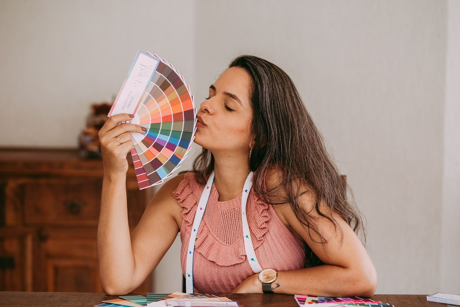Designer morena segurando um leque de cores vibrantes em um estúdio criativo