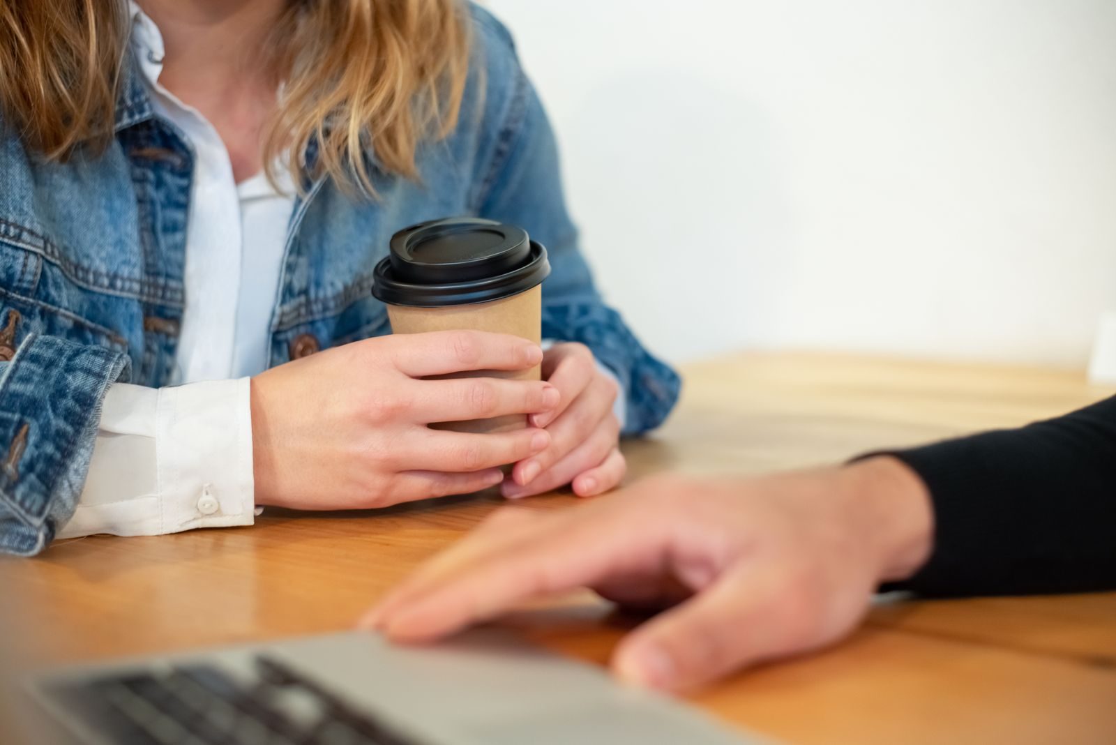 Close de duas pessoas tomando café e trabalhando em um notebook em uma mesa de madeira