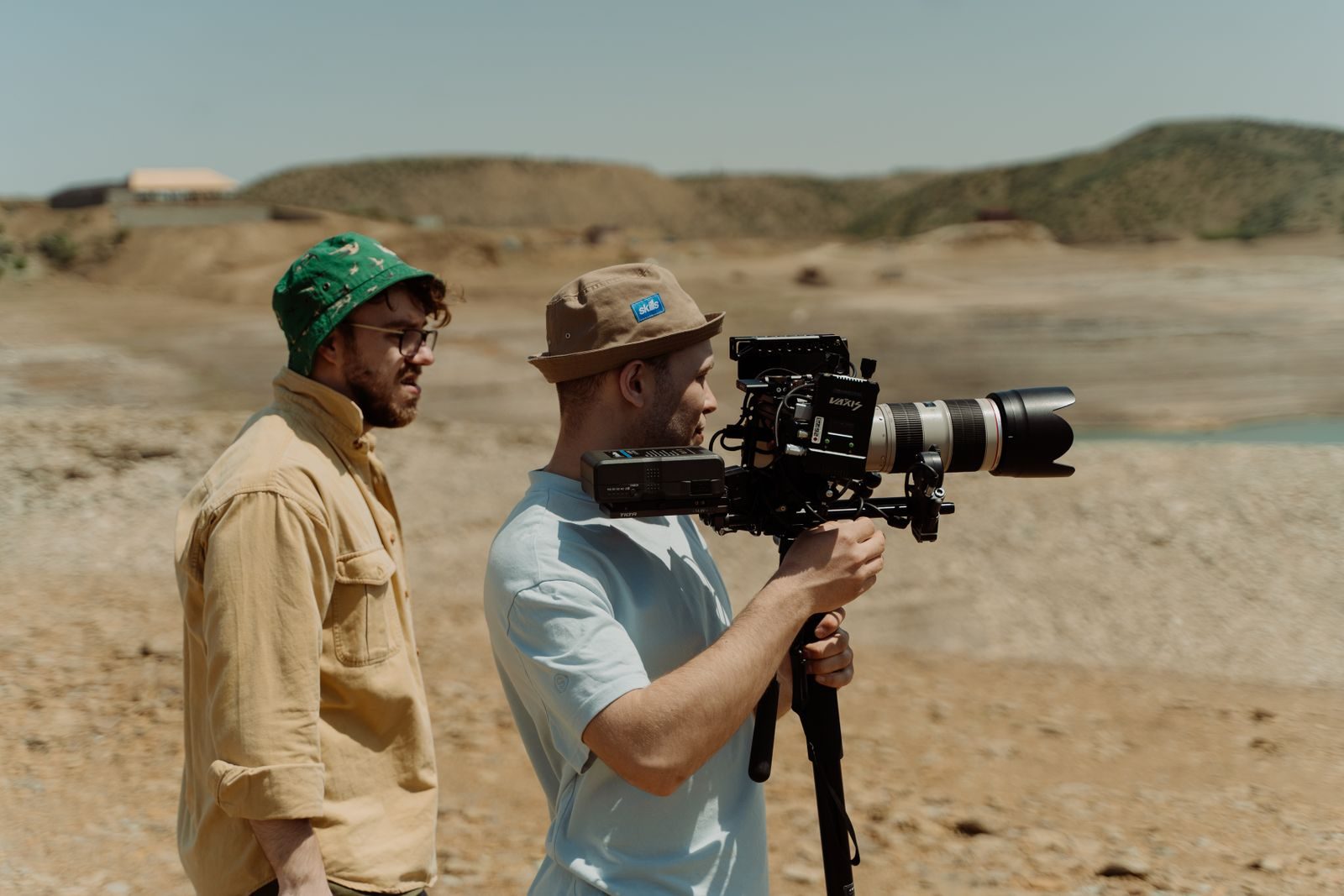 Dois cineastas operando uma câmera de vídeo profissional em uma paisagem rochosa