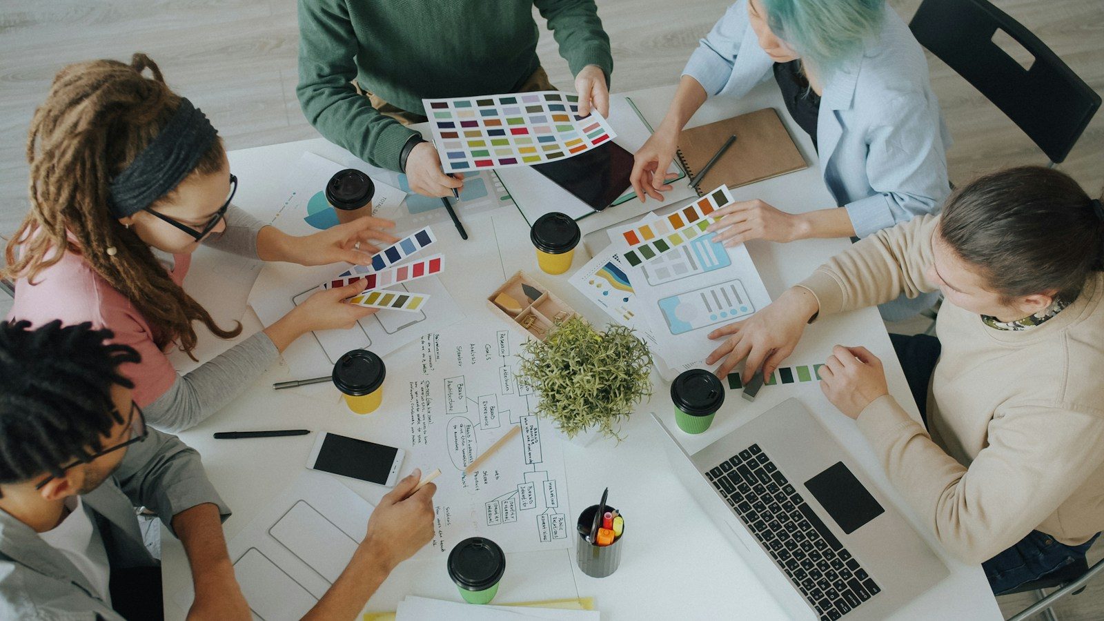 Grupo de pessoas trabalhando juntas em projetos de design em uma mesa branca