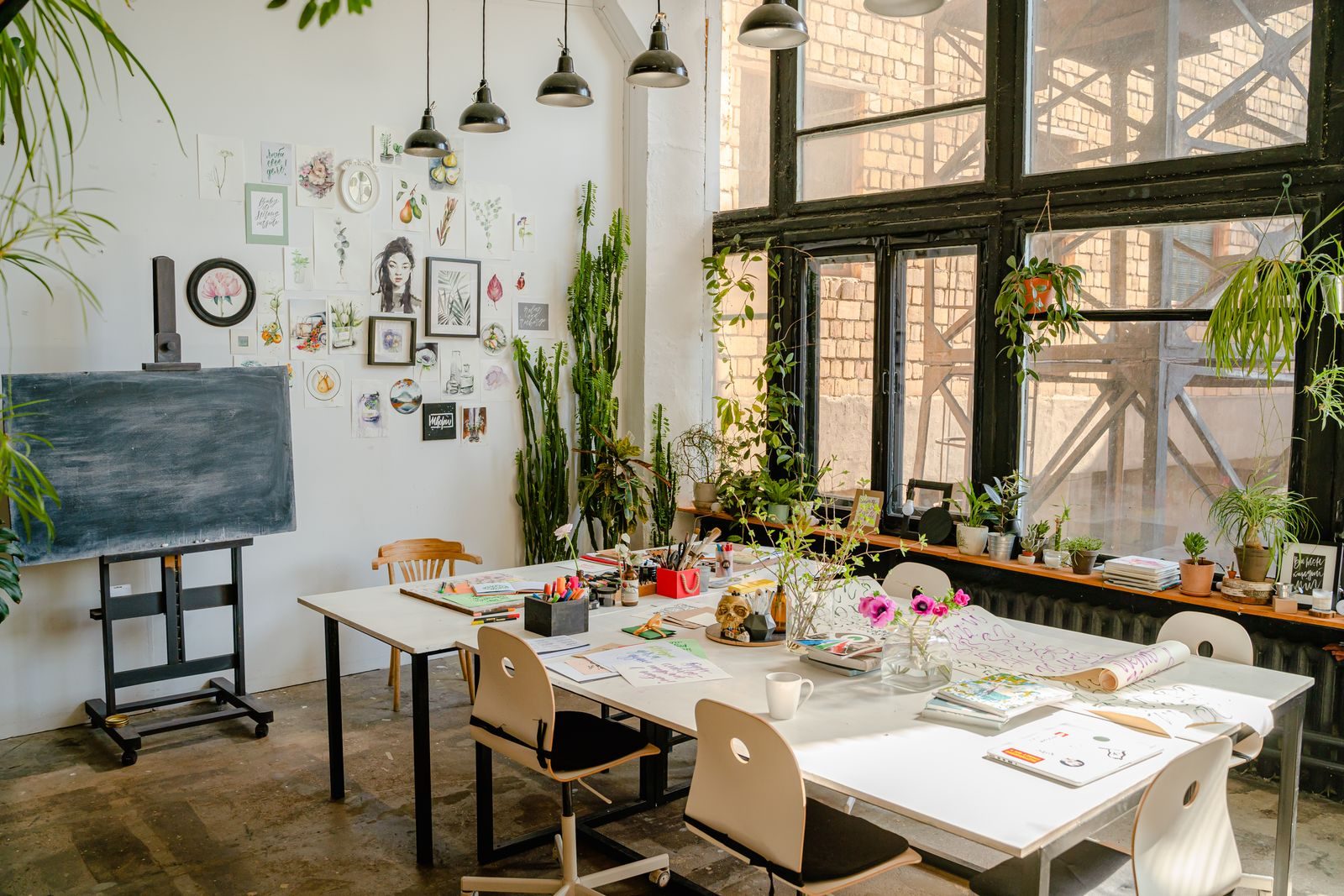 Estúdio de arte iluminado com mesas, plantas e diversos materiais artísticos