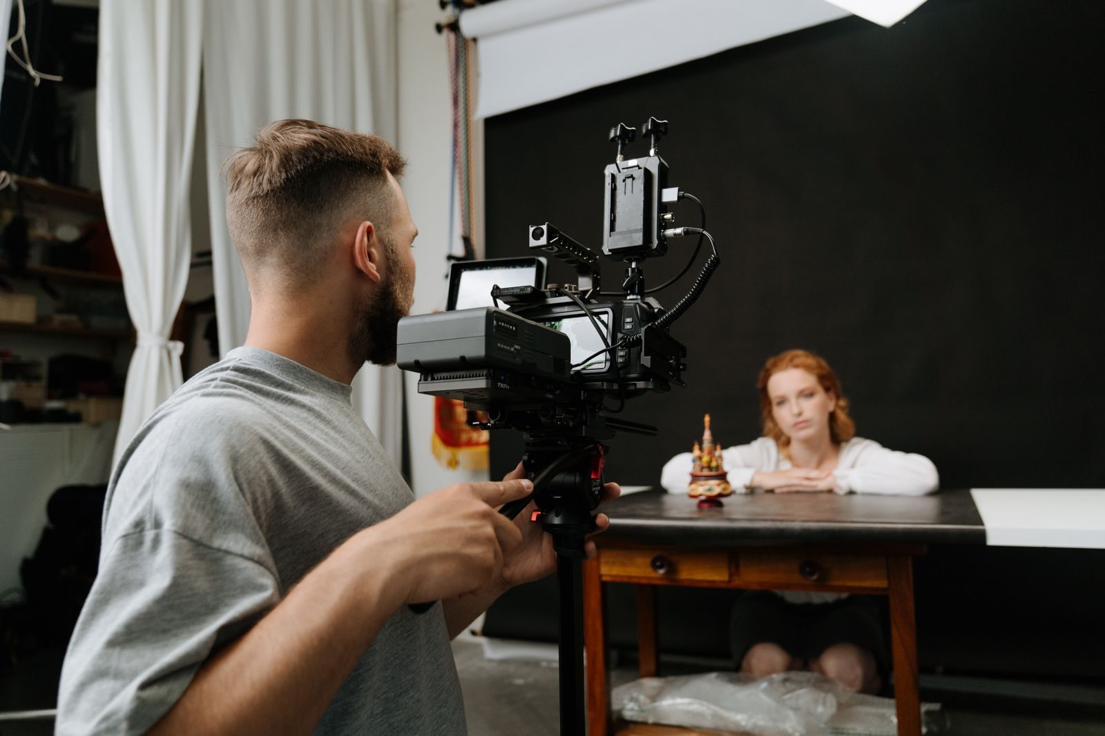 Cinegrafista filmando mulher ruiva em estúdio com fundo escuro