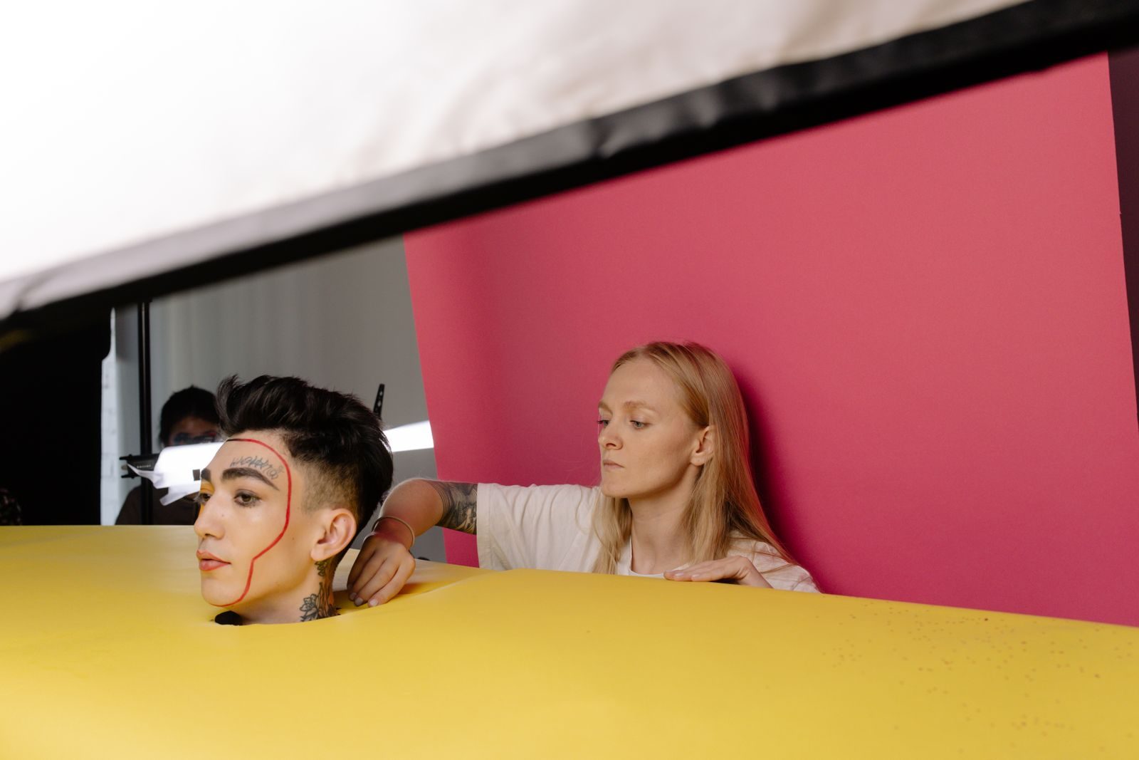 Bastidores de ensaio em estúdio com modelo de maquiagem artística e fundo vibrante
