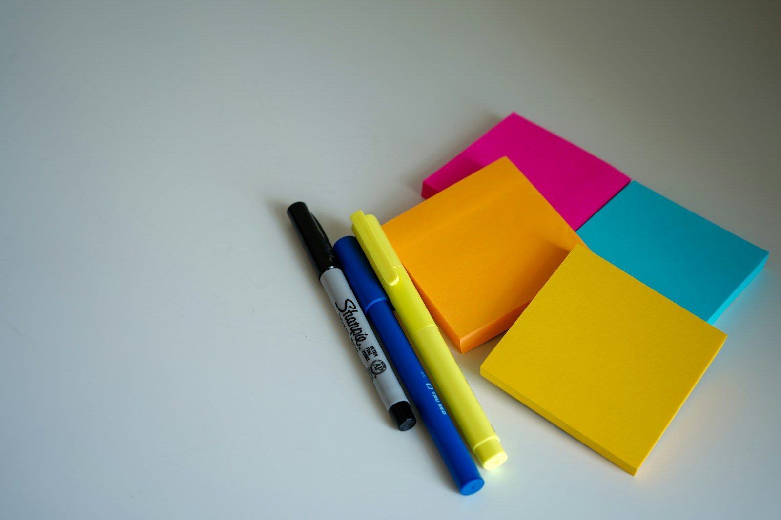 Caneta azul e preta ao lado de post-its laranja