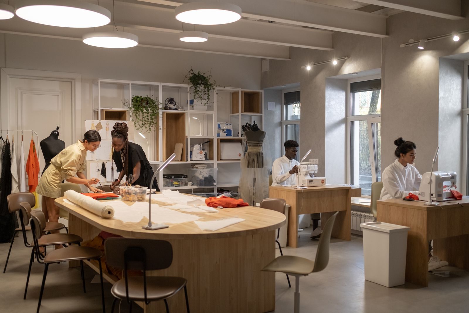 Estilistas trabalhando juntos em um ateliê moderno com máquinas de costura e moldes