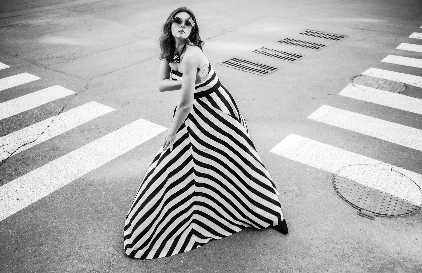 Mulher de vestido longo listrado e óculos de sol posando em uma faixa de pedestres