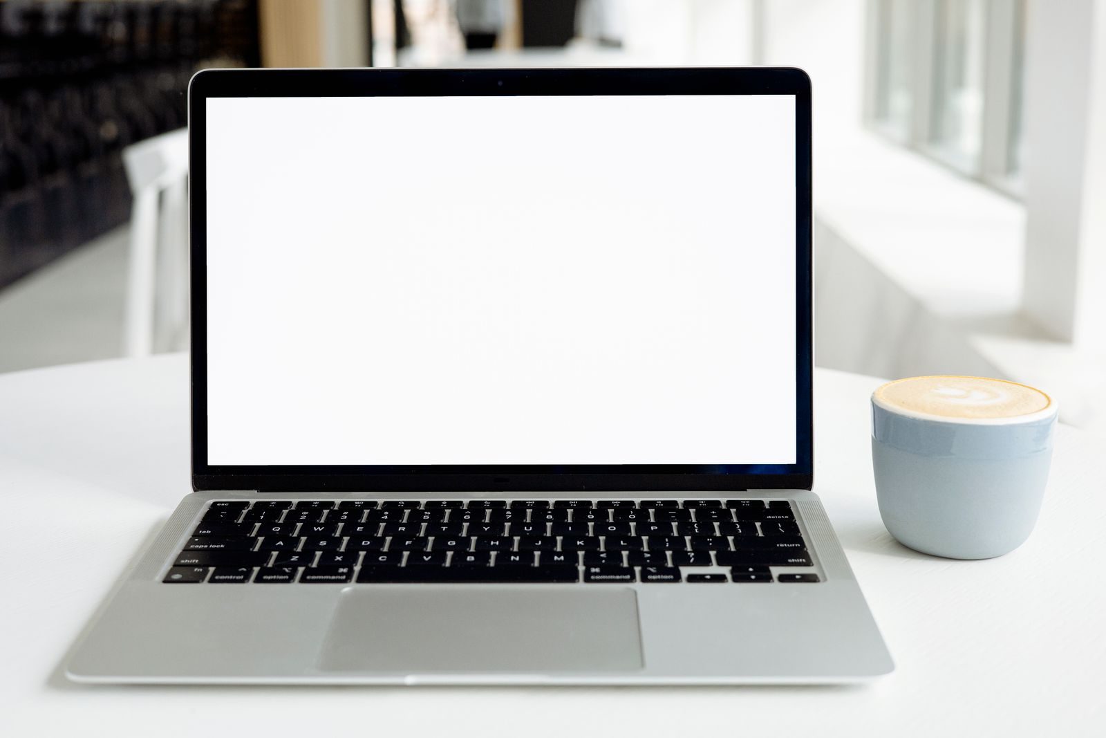 Espaço de trabalho minimalista com notebook de tela em branco e um cappuccino em ambiente moderno