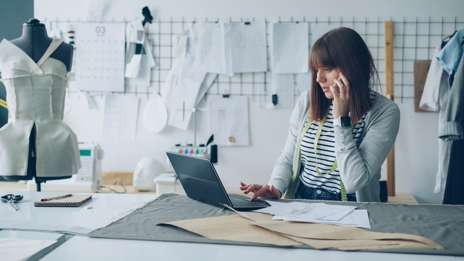 Estilista trabalha no notebook enquanto fala ao telefone