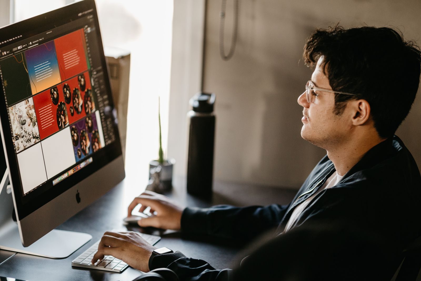 Designer gráfico concentrado trabalhando no computador em escritório moderno com imagens criativas na tela