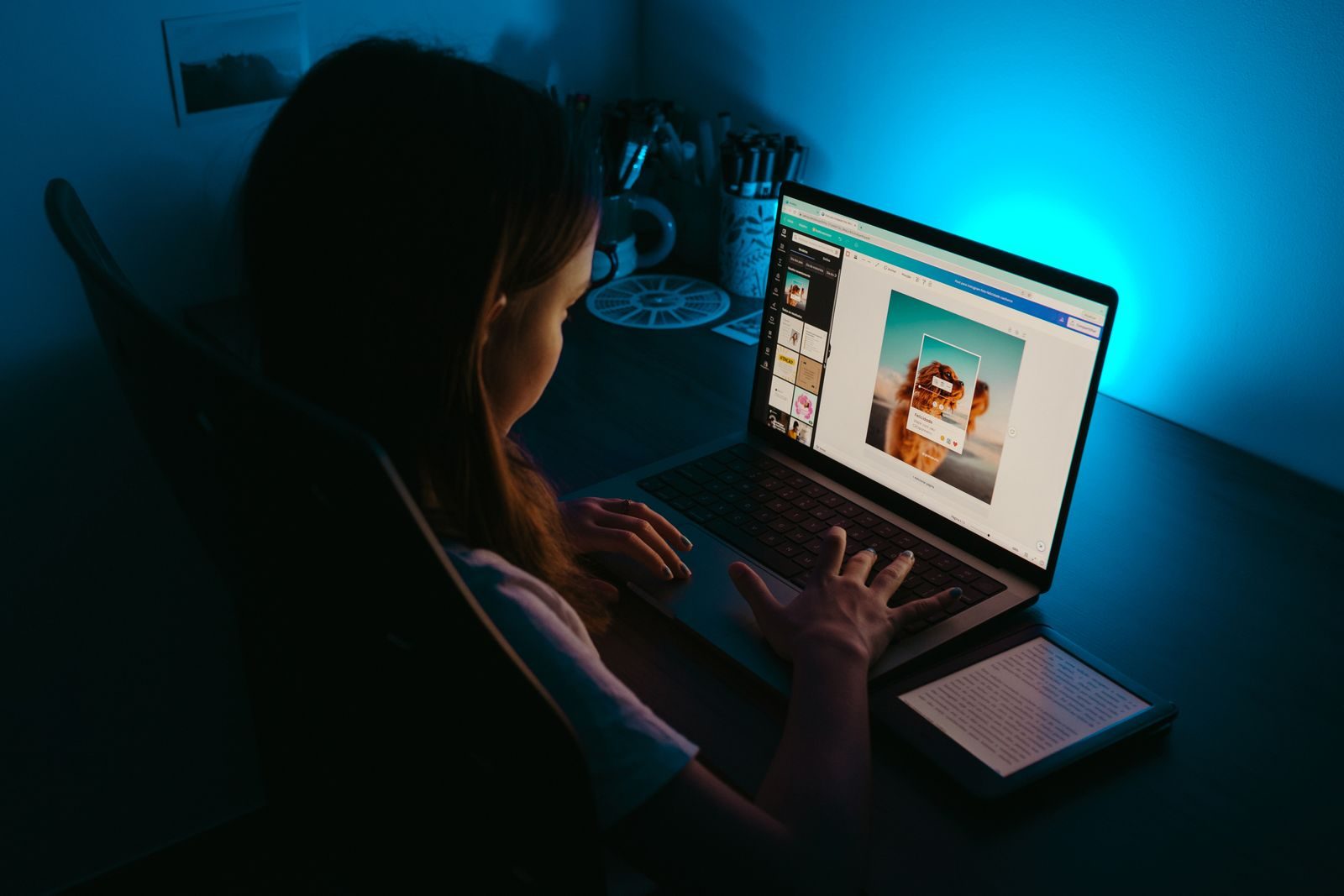 Garota usa notebook em uma mesa em quarto com pouca luz e iluminação azul tranquila