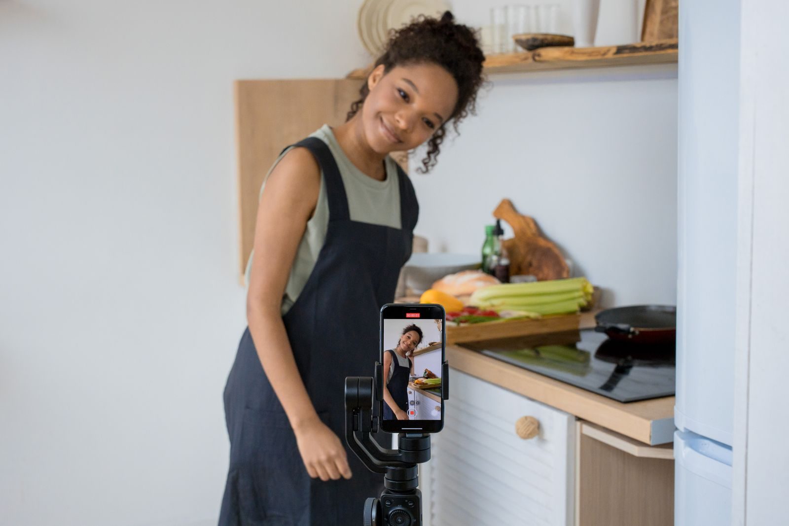 Jovem sorridente gravando vídeo de culinária com smartphone na cozinha de casa