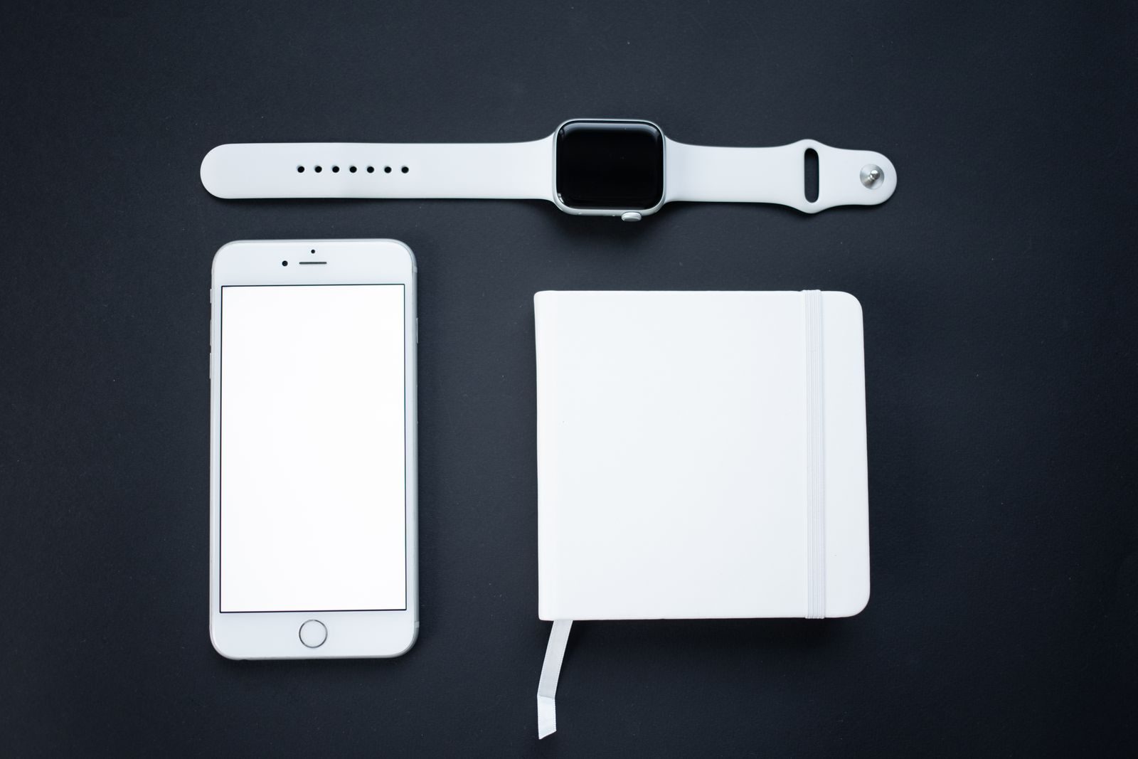 Vista de cima minimalista de smartphone, smartwatch e bloco de notas sobre fundo escuro