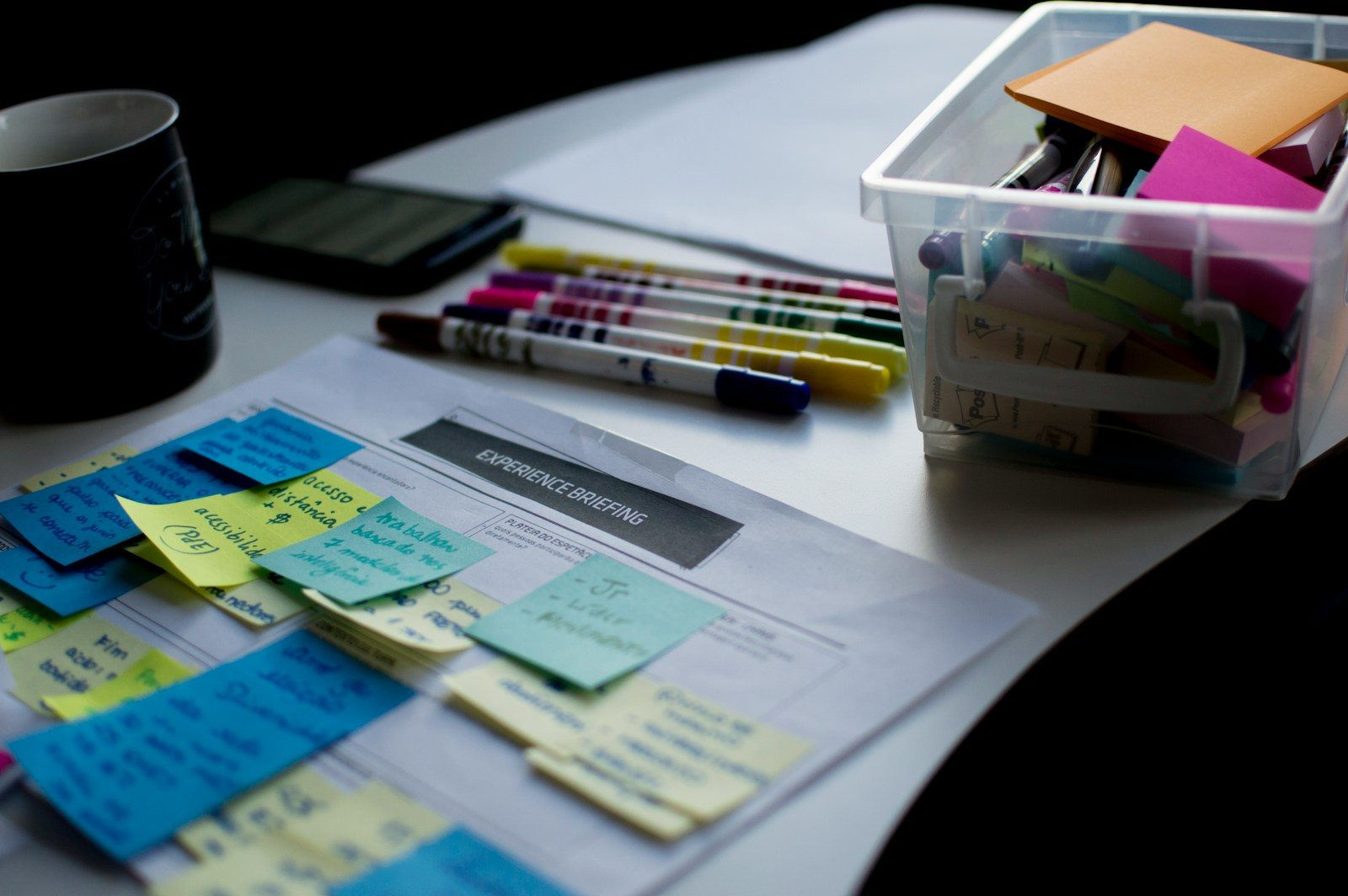 Post-its sobre documento ao lado de canetas e uma caixa