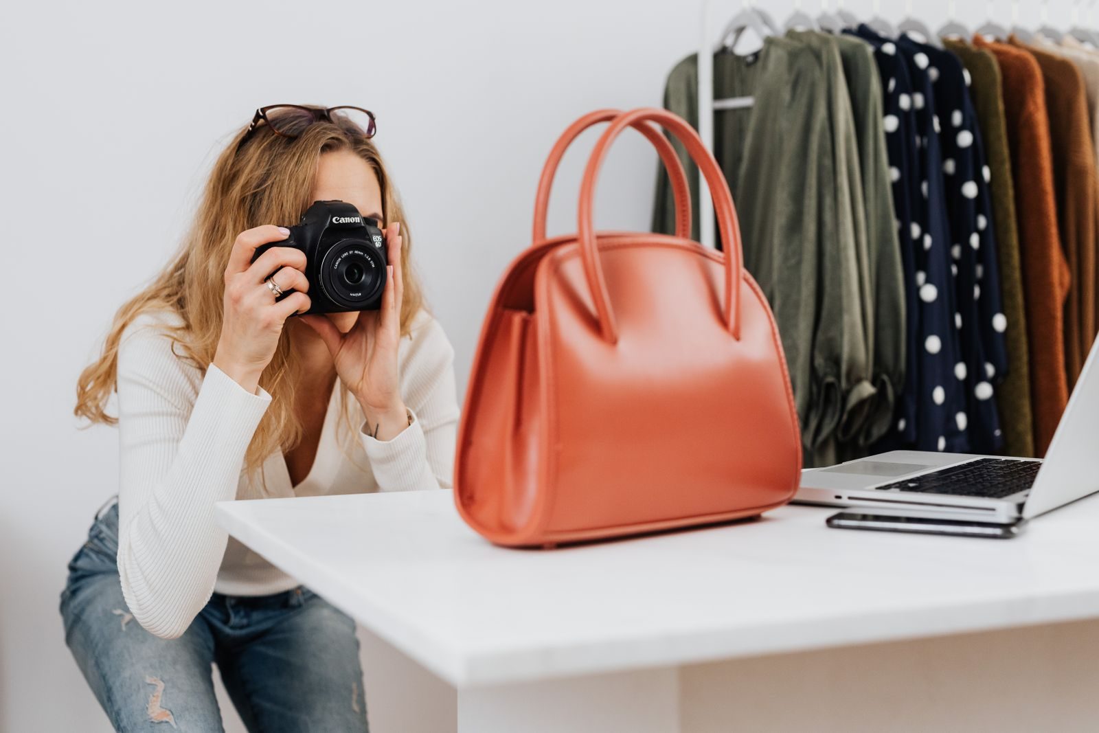 Mulher branca fotografando bolsa com câmera para loja de moda online