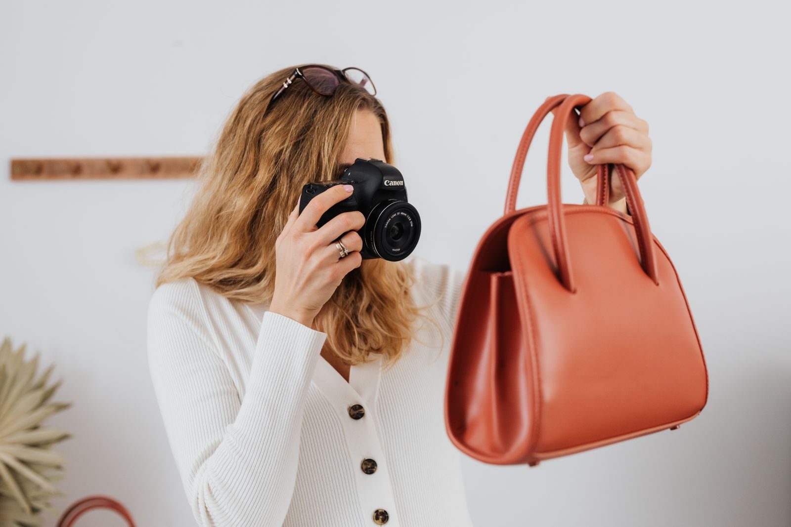 Mulher de blusa branca de mangas longas fotografando uma bolsa para venda online