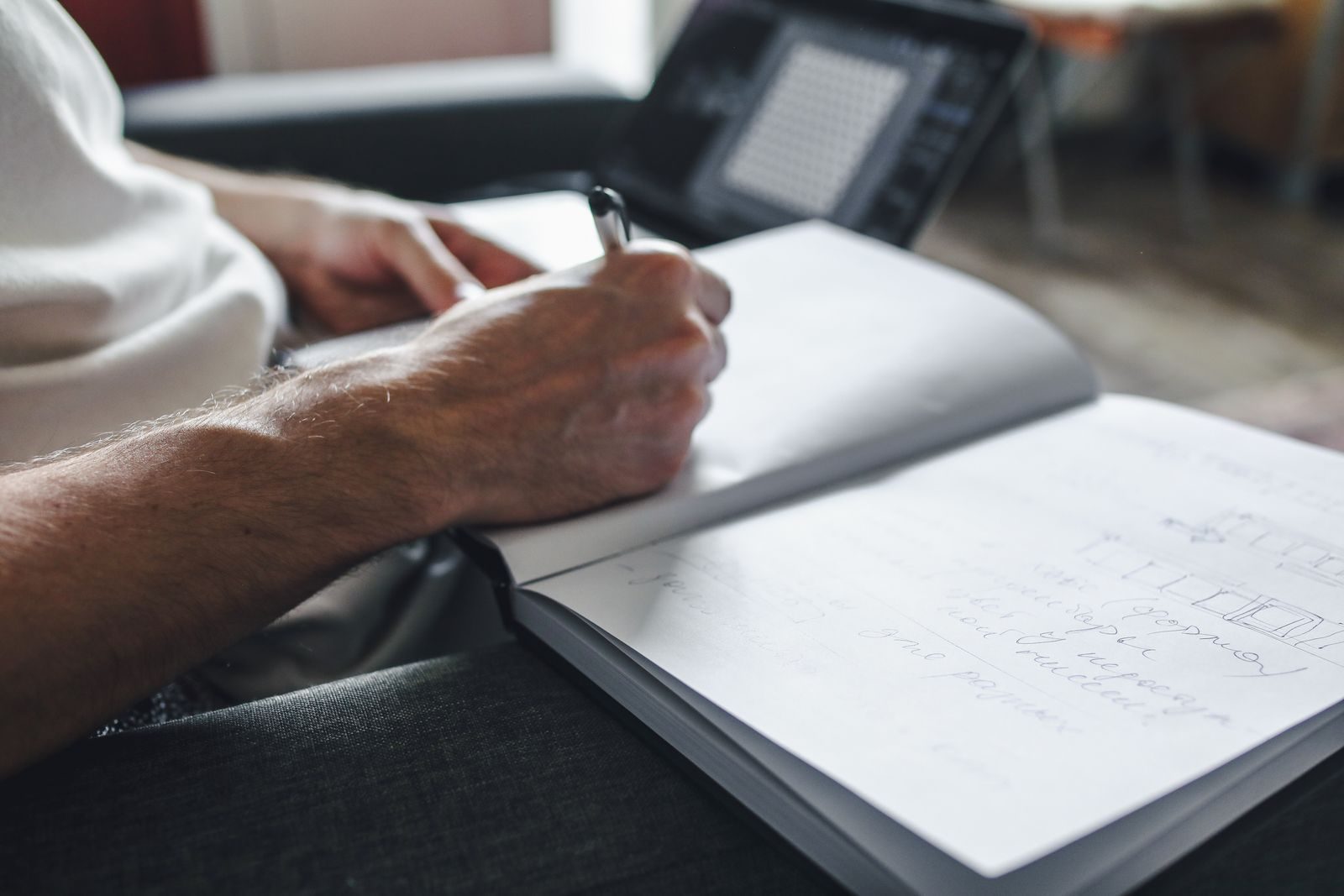 Pessoa concentrada fazendo anotações em caderno com notebook ao lado