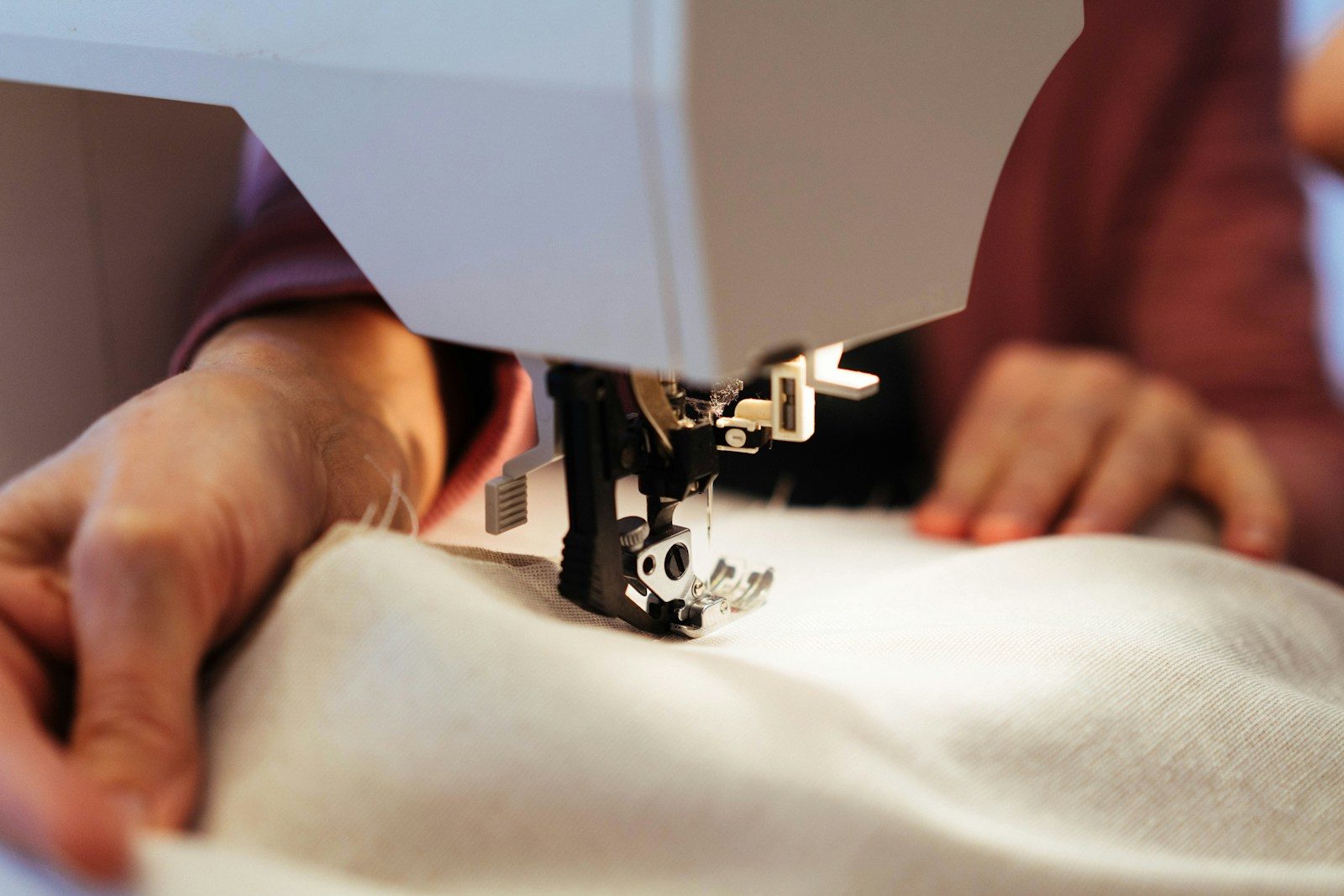 Mãos operando uma máquina de costura sobre tecido