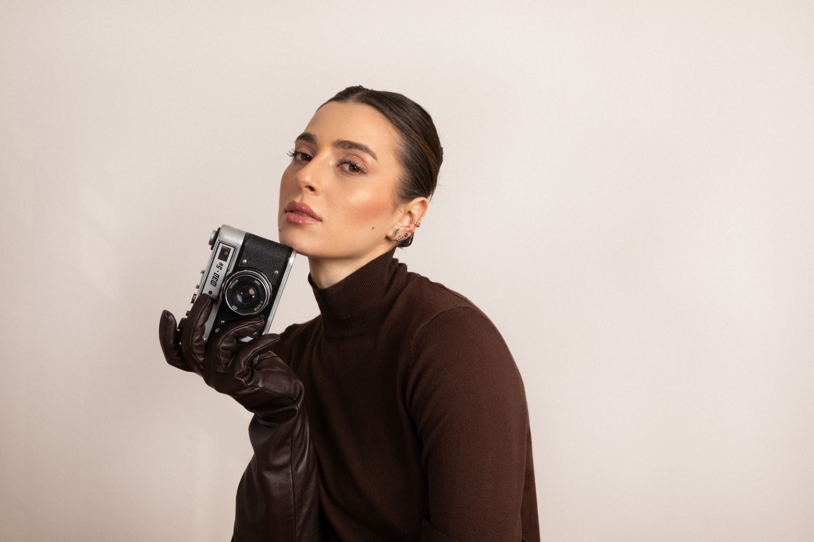 Mulher elegante de gola alta marrom posando com câmera vintage