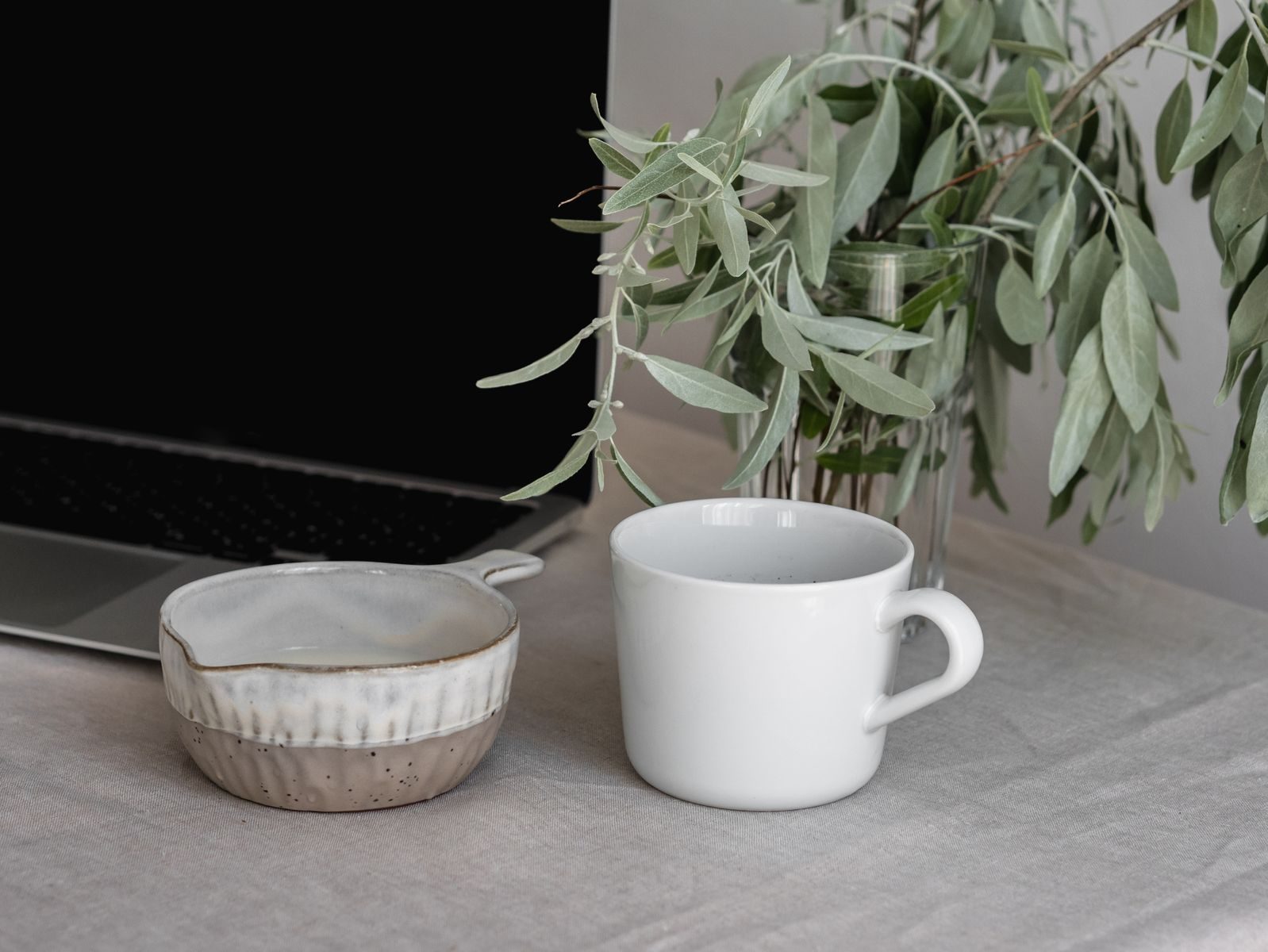 Espaço de trabalho tranquilo com caneca de cerâmica, tigela e vaso com planta sobre toalha neutra