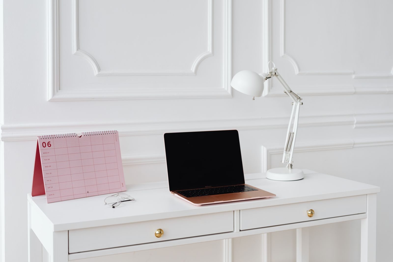 Mesa simples com notebook, calendário e luminária em um escritório minimalista e iluminado