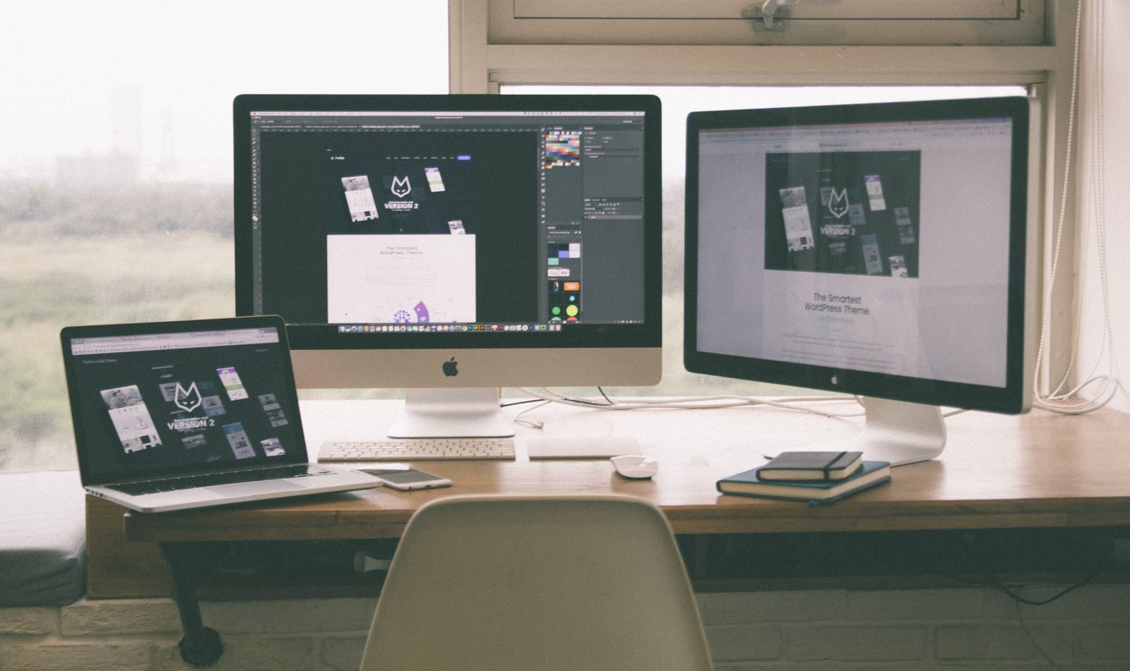 Espaço de trabalho com vários monitores, notebook e smartphone mostrando um projeto de web design