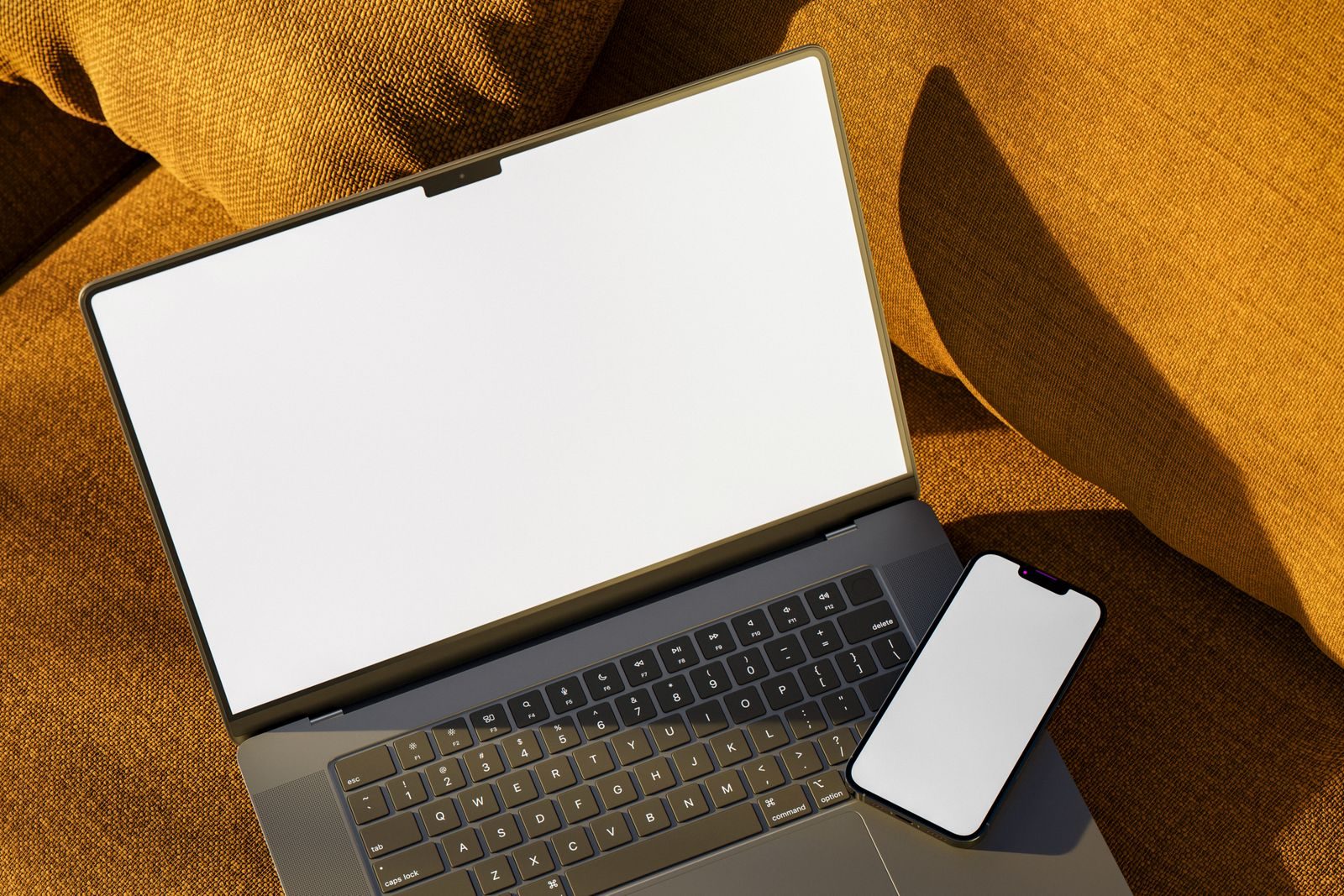 Vista de cima de notebook e smartphone com telas em branco em um sofá sob luz quente