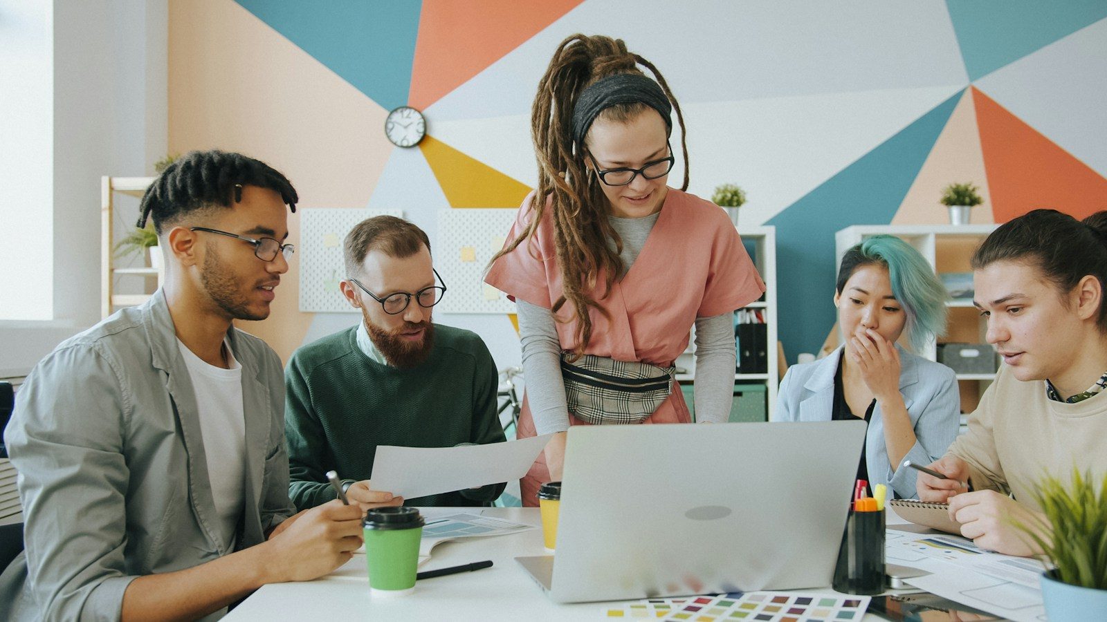 Cinco pessoas colaborando em volta de um notebook em escritório colorido