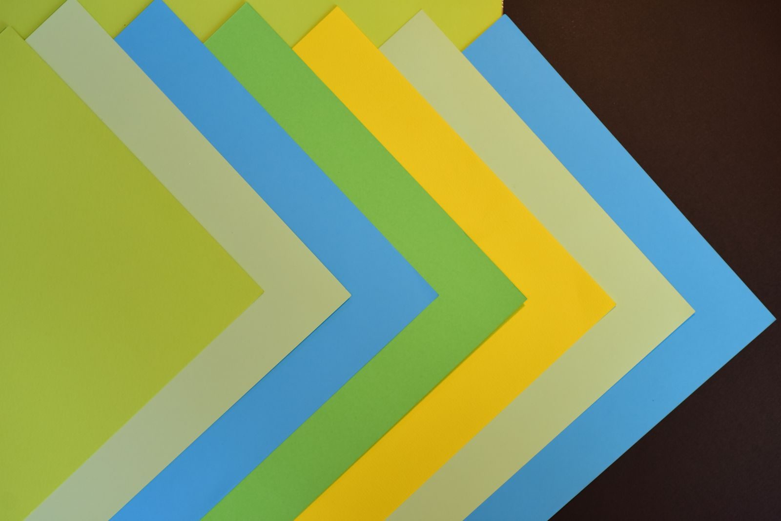 Folhas de papel coloridas formando padrão geométrico sobre superfície marrom