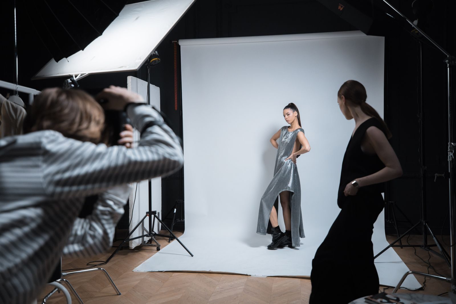 Ensaio profissional em estúdio com modelo de vestido prateado, fotógrafo e assistente