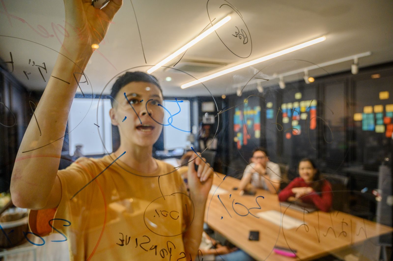 Equipe fazendo brainstorming em quadro transparente em escritório moderno
