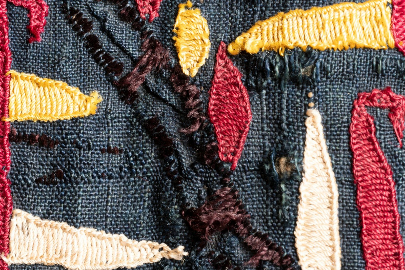 Close de tecido escuro com formas abstratas bordadas em cores vivas