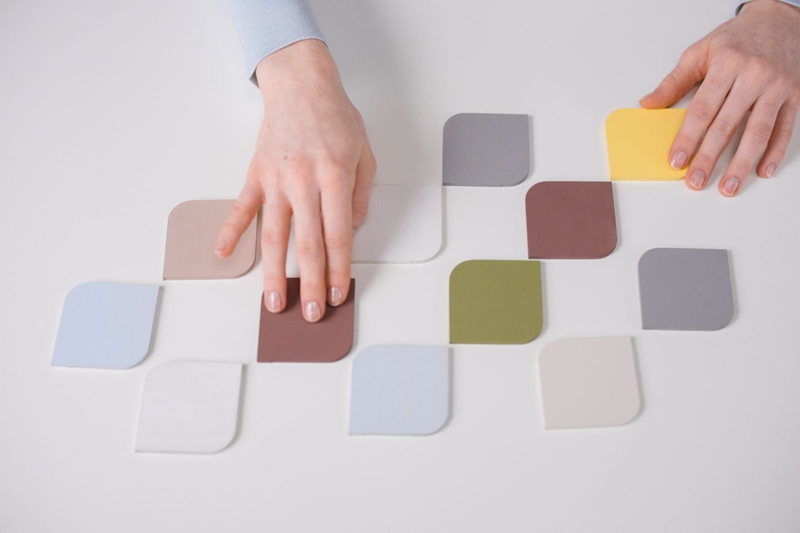 Mãos organizando amostras coloridas sobre mesa branca minimalista