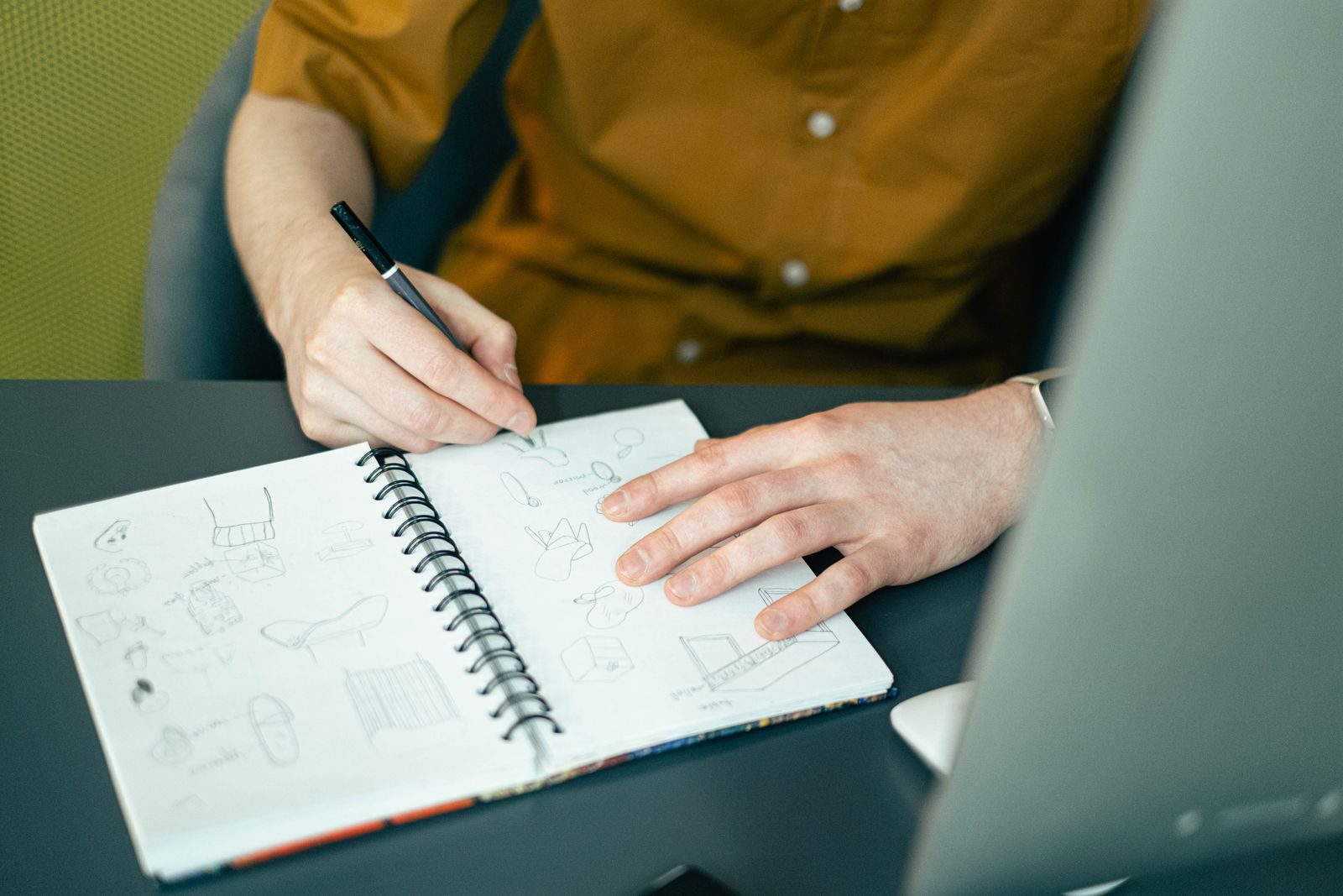 Close de designer esboçando ideias em caderno espiral sobre uma mesa