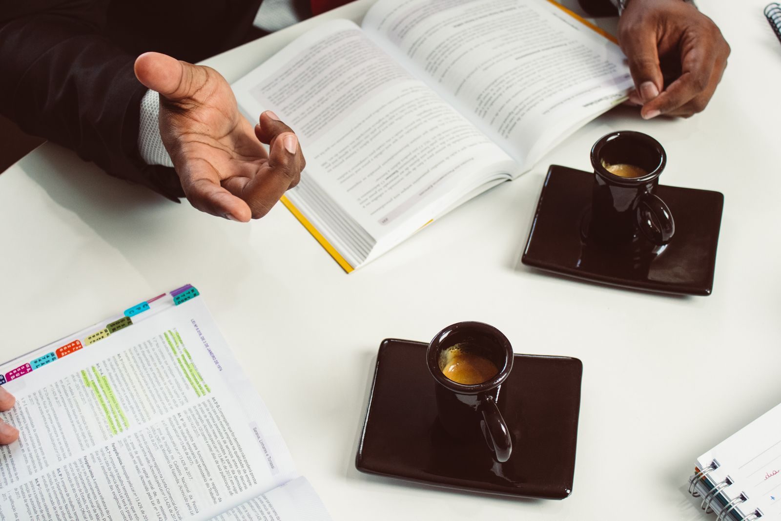 Reunião formal com xícaras de espresso e livros abertos em escritório de São Paulo