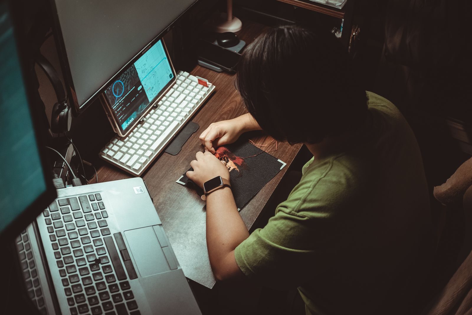 Pessoa fazendo trabalho artístico detalhado em mesa de home office com aparelhos tecnológicos