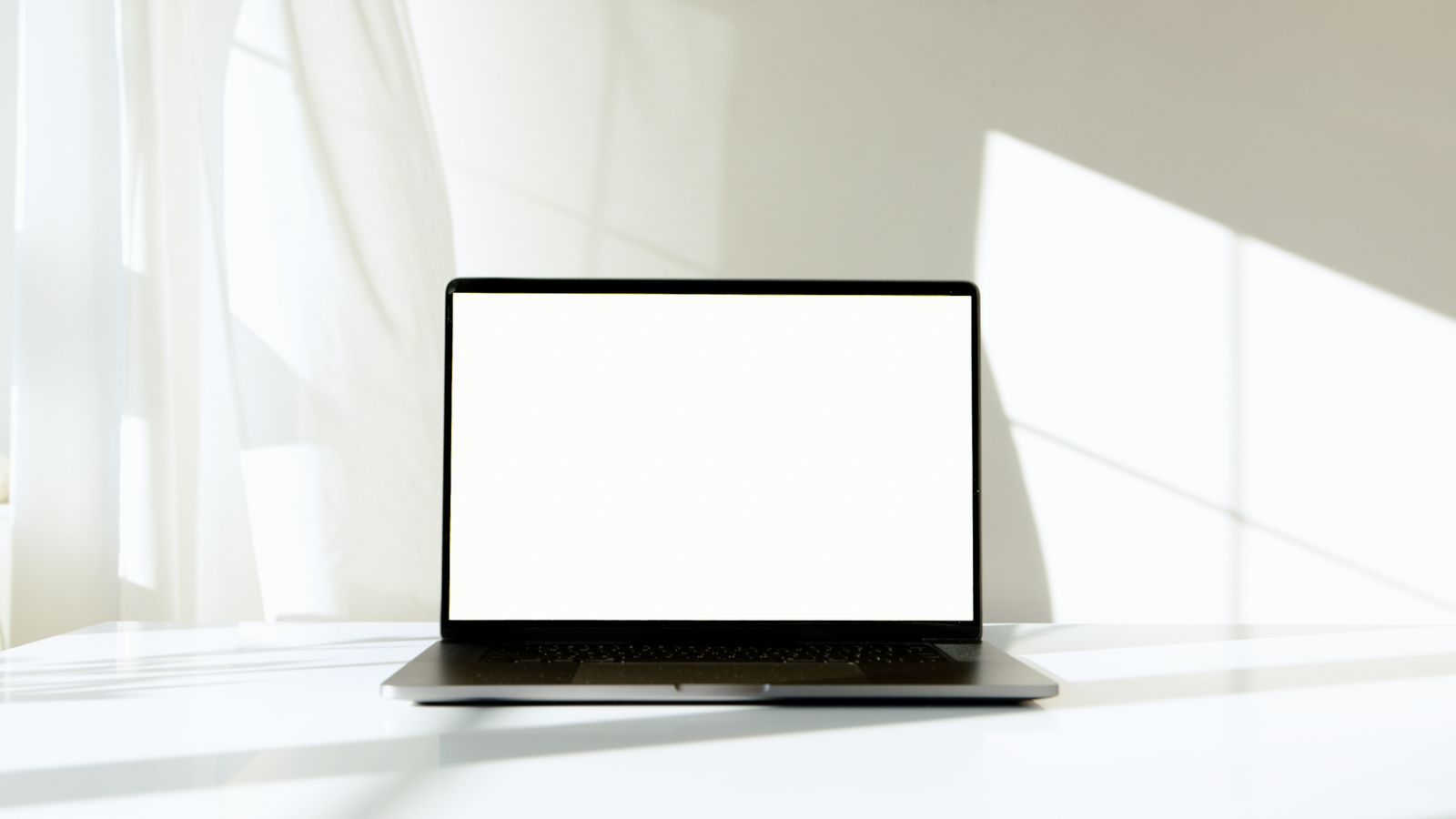 Notebook minimalista com a tela apagada sobre mesa branca, sob luz natural