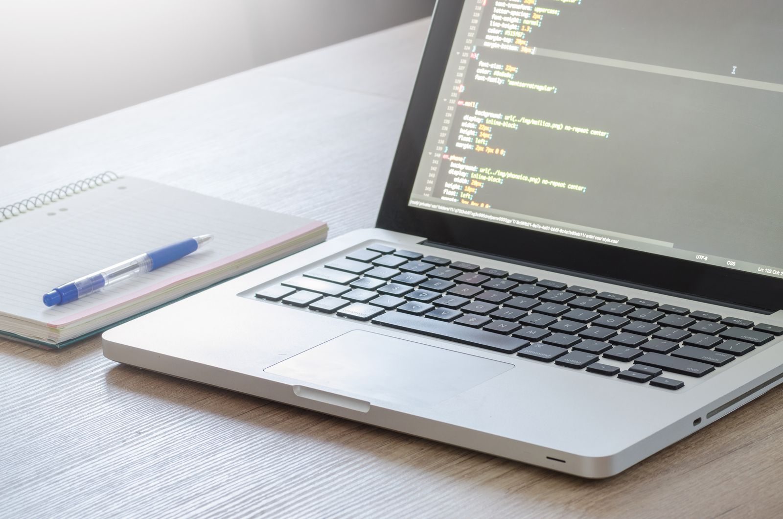 Notebook com editor de código aberto, caderno e caneta sobre mesa de madeira